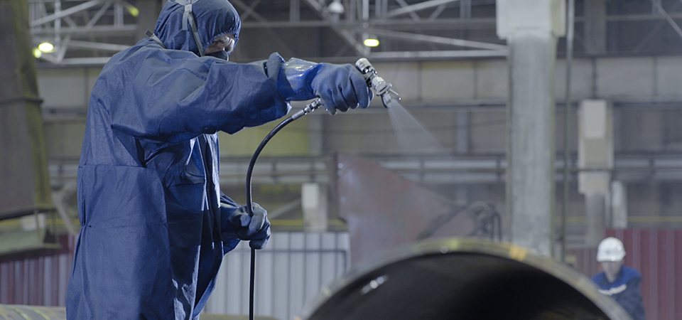 Male holding spray gun and painted steel. Man paints pipe atomizer.